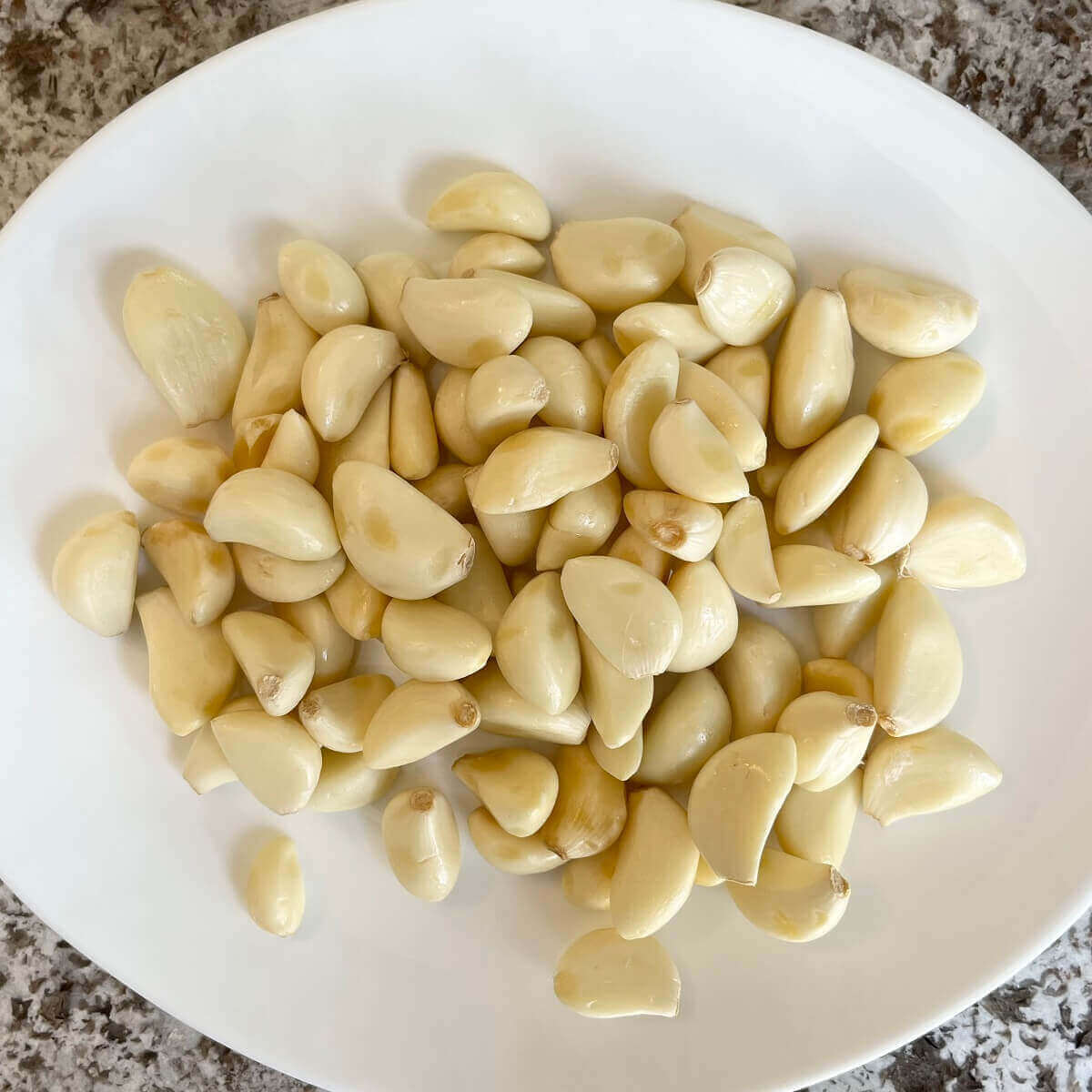 A pile of peeled garlic cloves on a white plate.