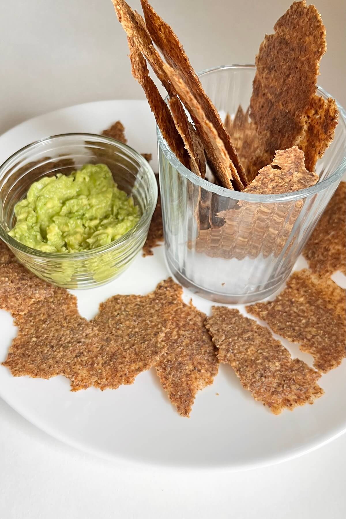 Flax crackers next to a glass dish of guacamole.