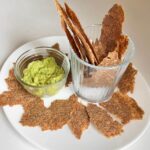 Vegan flaxseed crackers next to a dish of guacamole.