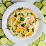Hummus in a white dish surrounded by cucumber slices.