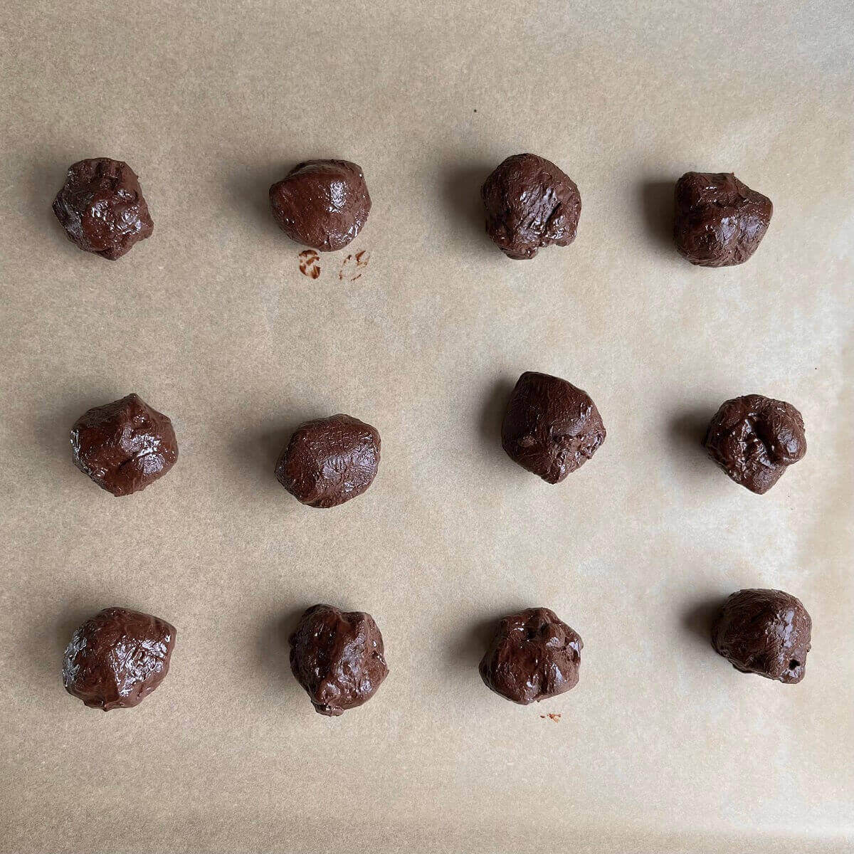 Twelve tahini chocolate balls on a sheet pan lined with parchment paper.