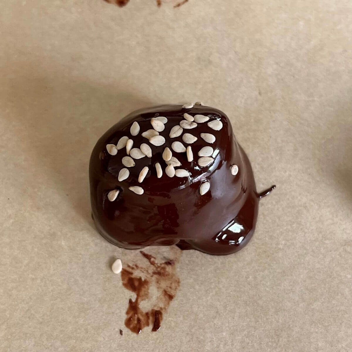 A chocolate dipped tahini ball sprinkled with sesame seeds on a sheet pan lined with parchment paper.