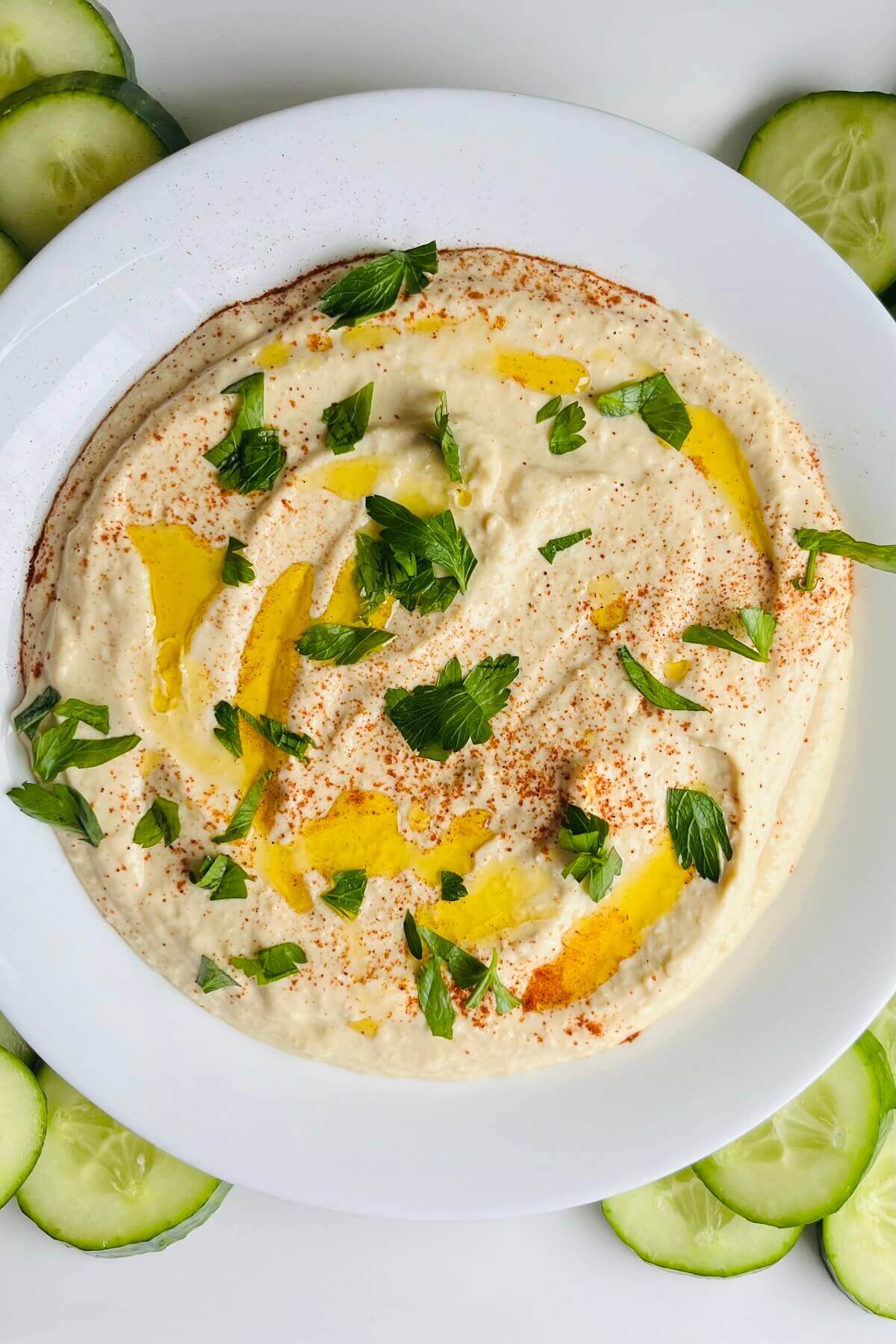 Hummus in a white dish garnished with fresh parsley.