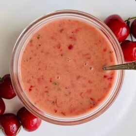 Cherry dressing in a glass bowl surrounded by fresh cherries.