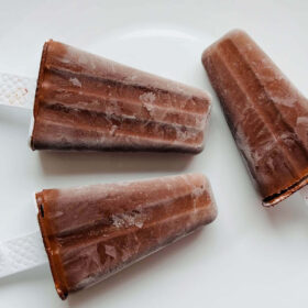 Three dark chocolate popsicles on a white plate.