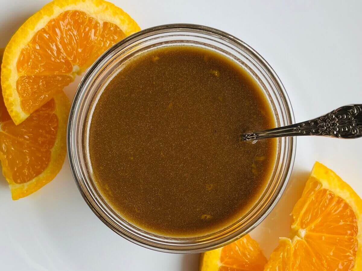 Orange dressing in a glass bowl with a silver spoon.