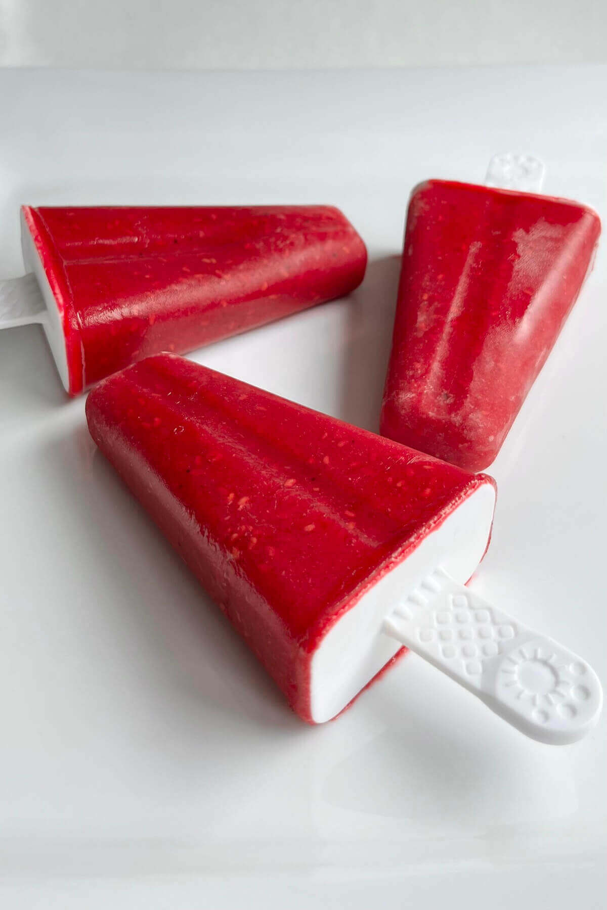 Three popsicles made with raspberries on a white plate.