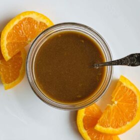 Orange balsamic salad dressing in a glass bowl next to some orange slices.