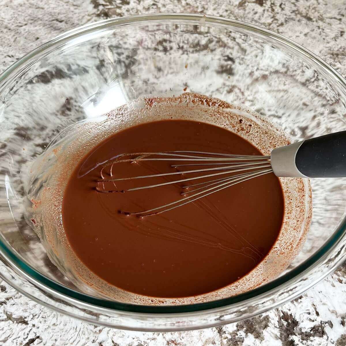 Ingredients for popsicles being mixed with a whisk in a glass bowl.