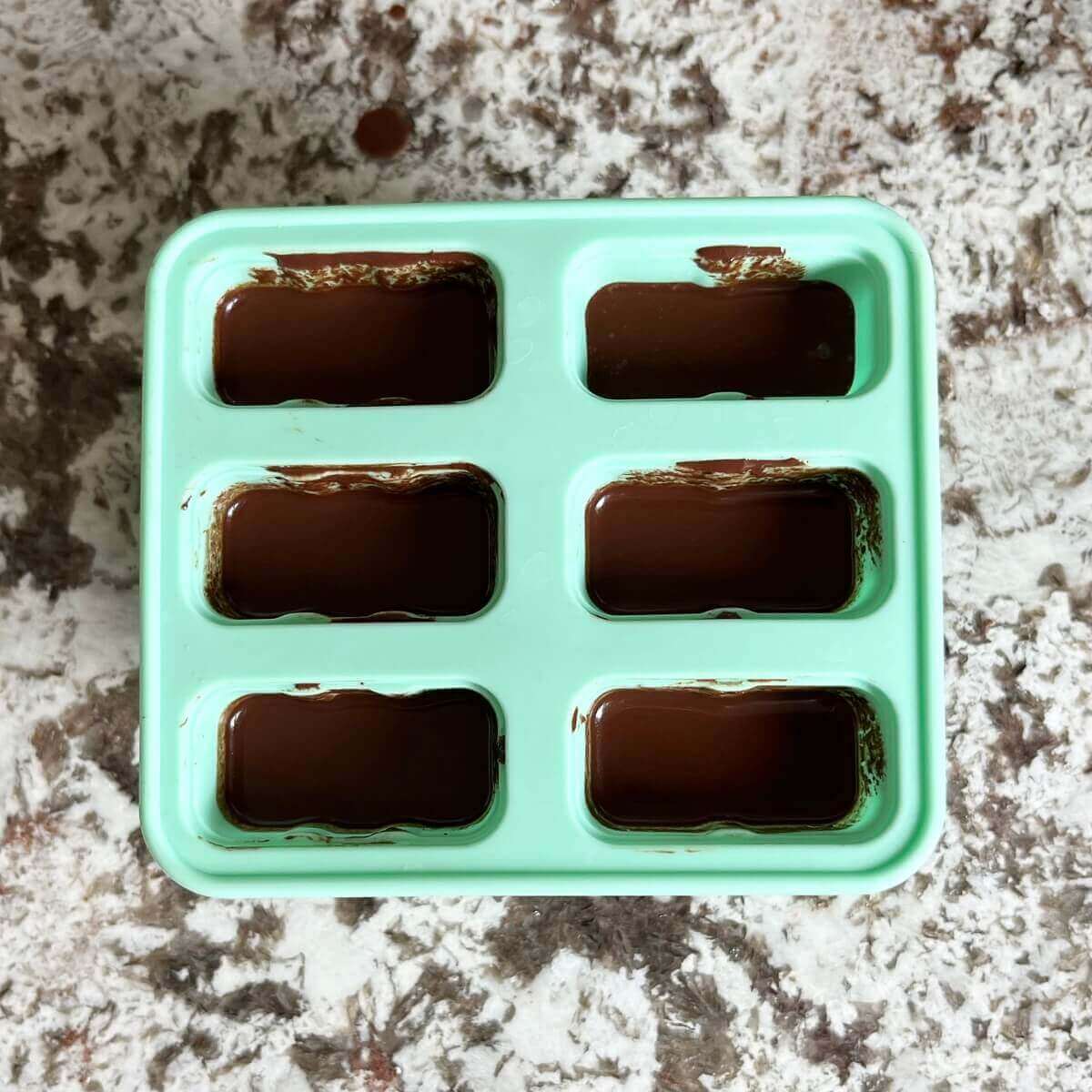 A popsicles mold with chocolate batter in each slot.
