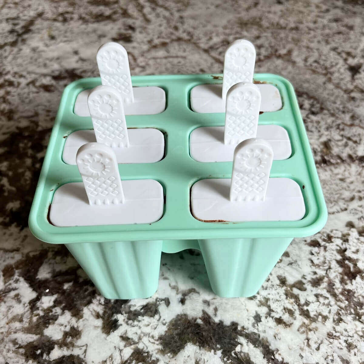 A turquoise popsicle mold on a granite counter.