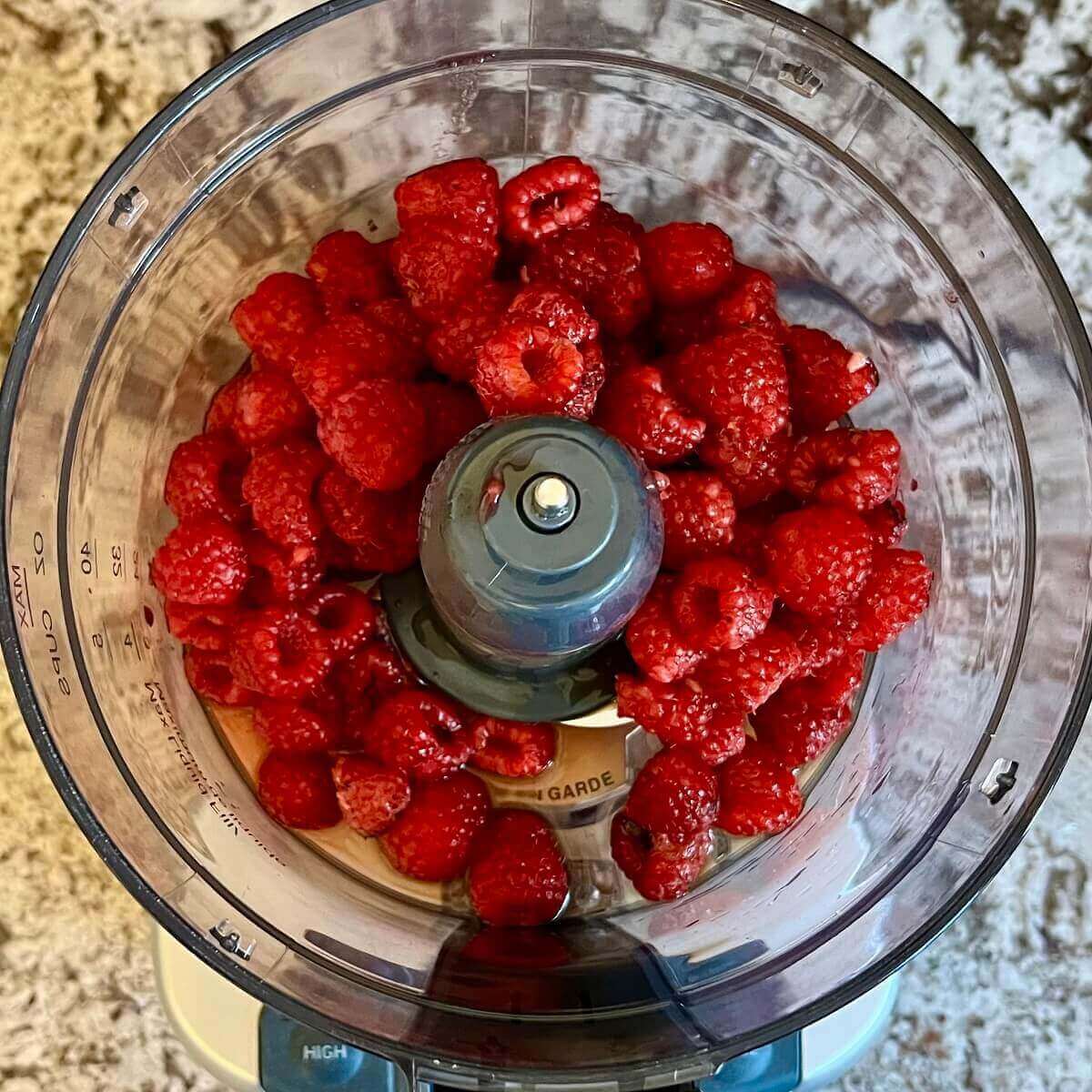 Raspberries and other ingredients for popsicles in a food processor.
