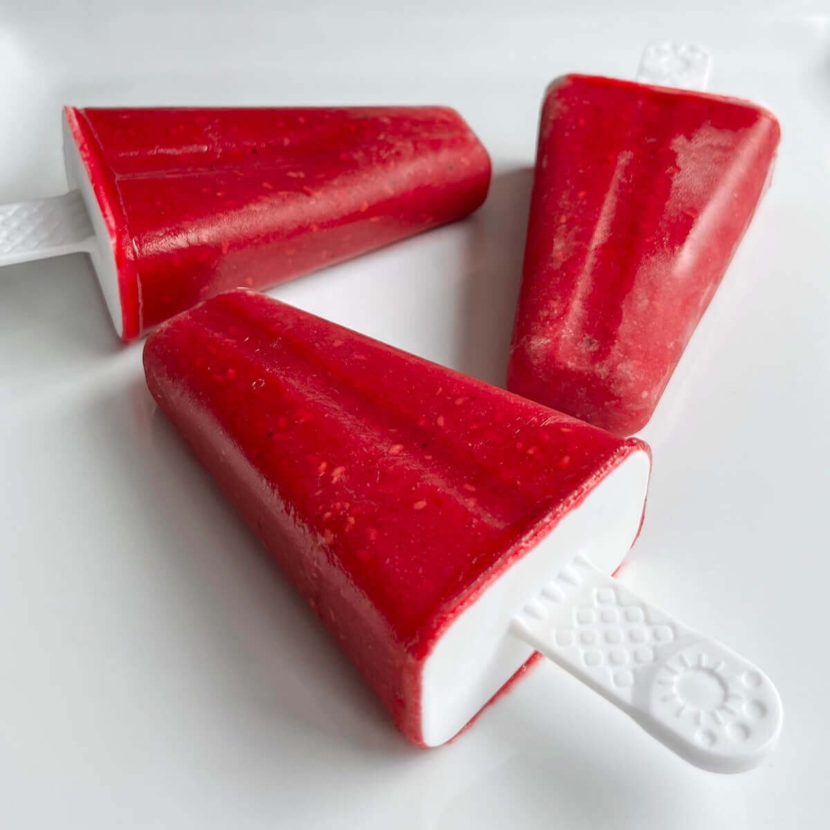 Three raspberry popsicles on a white plate.