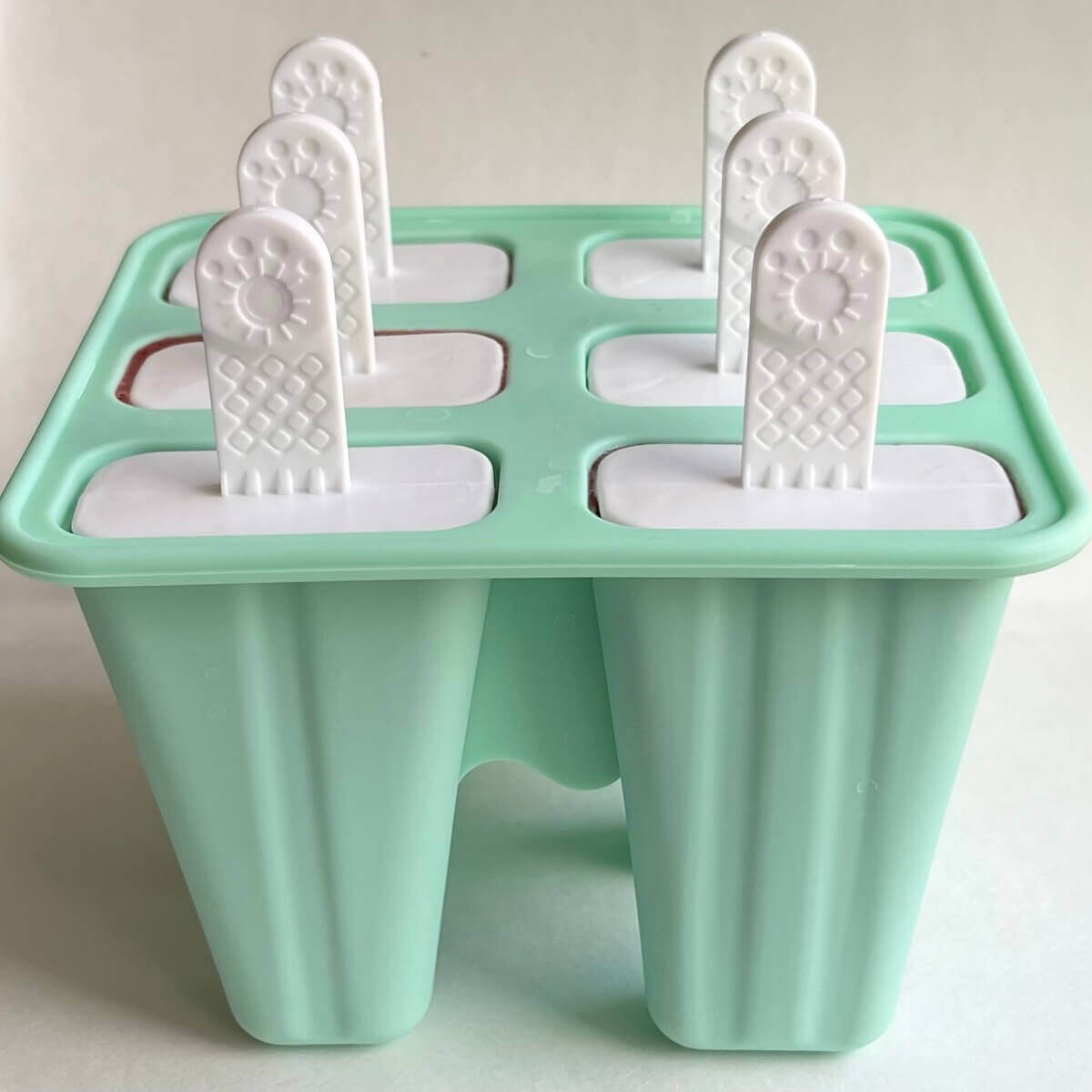 A turquoise popsicle mold with white popsicle sticks.