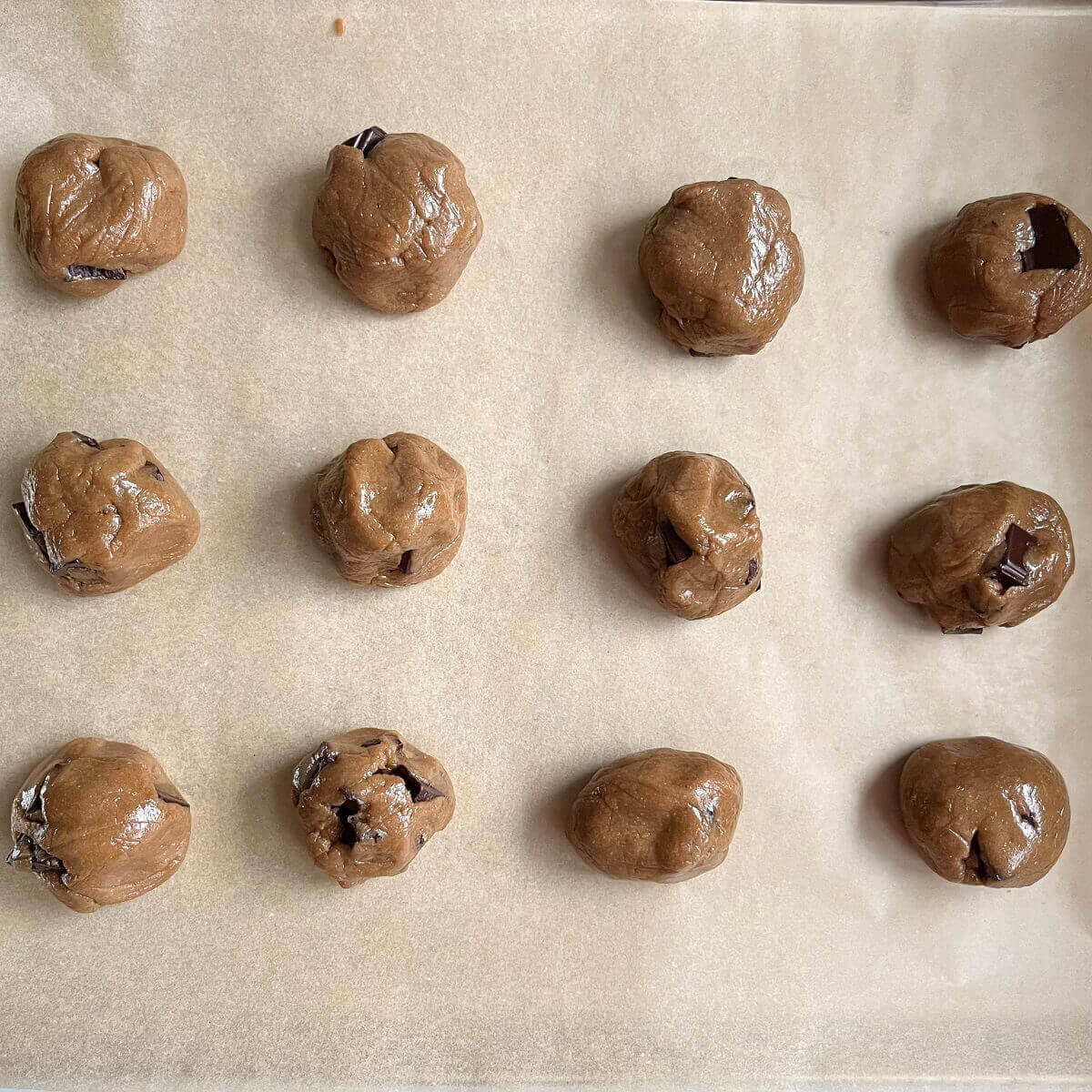 Sunflower seed butter cookie dough balls on a baking sheet lined with parchment paper.